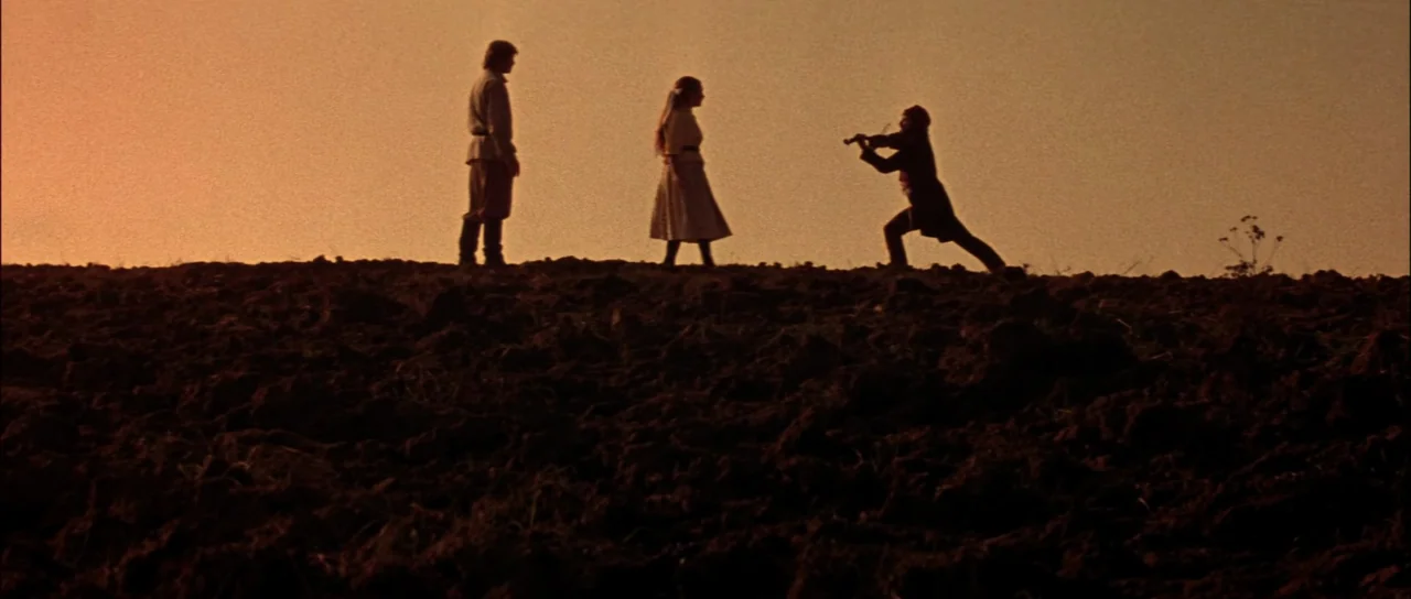 Fiddler On The Roof (1971) movie still: wide — A dark, uneven expanse of plowed earth occupies the lower portion of the frame. Three figures stand…