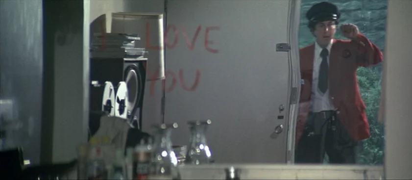 Nashville (1975) movie still: medium — The view through a glass panel shows a man entering a living space. The words 'I LOVE YOU' are written in red…