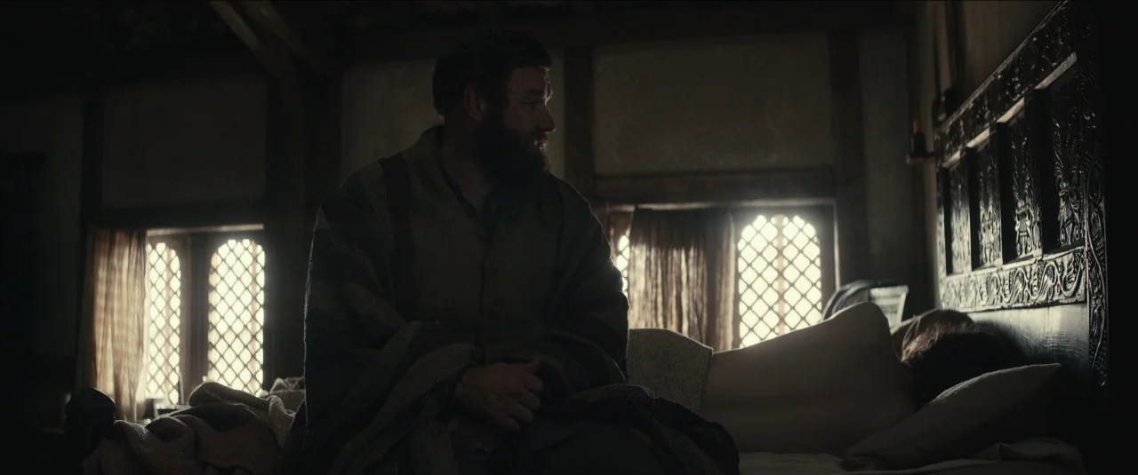 The King movie still: medium — A medieval room features exposed timber framing, diamond-pane lattice windows, and a dark carved headboard. A bearded…