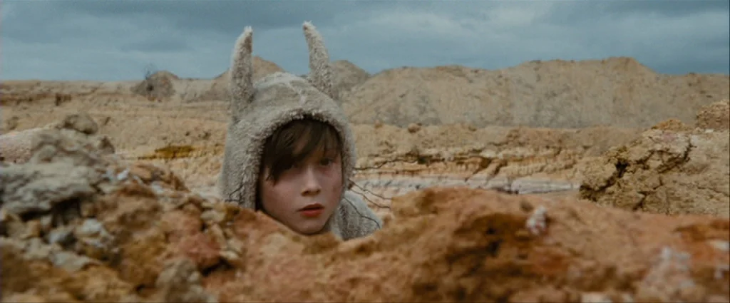 Where The Wild Things Are (2009) movie still: medium — An arid, rocky, and uneven desert landscape stretches out under a heavy overcast sky. A child…