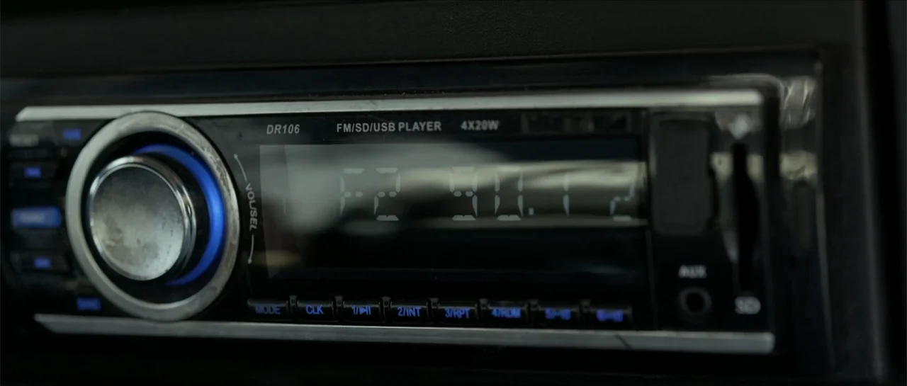 The Vault (2017) movie still: closeup — A close-up shot of a car's head unit with digital text visible. The radio display emits a faint blue light…