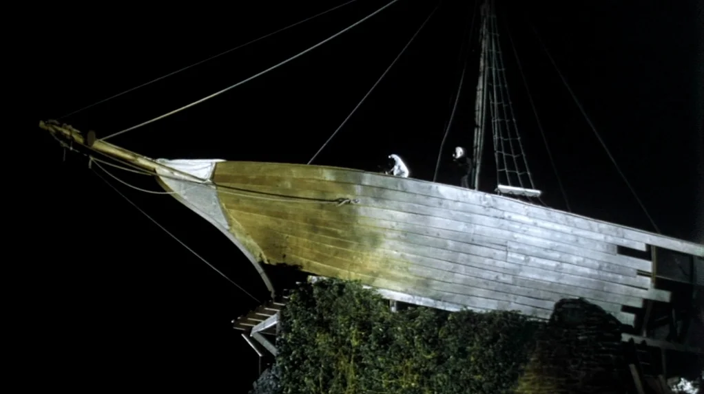 Shadow of the Vampire (2000) movie still: wide — A wooden ship bow rests on a dark rocky base at night. The ship is illuminated from the side while…