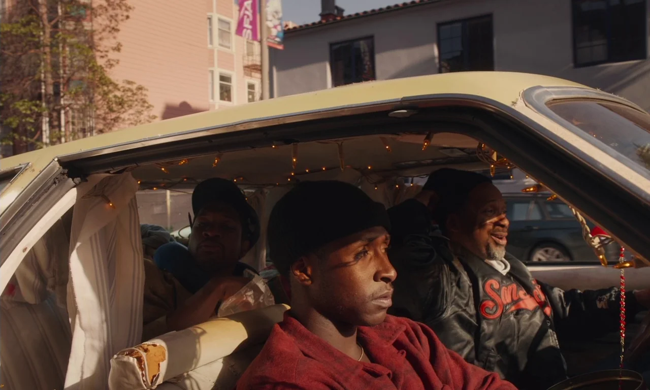The Last Black Man in San Francisco (2019) movie still: medium — Three men occupy the front of a vehicle with white curtains and string lights. They…