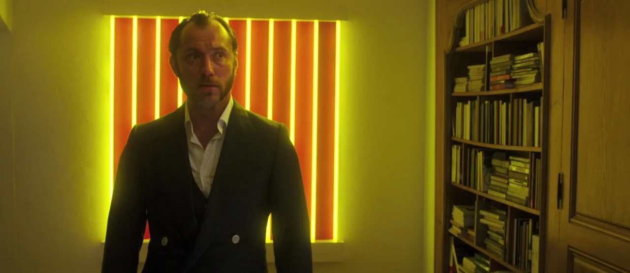Dom Hemingway (2013) movie still: medium — A dark study contains a tall wooden bookshelf filled with books and personal items. A man in a dark suit…