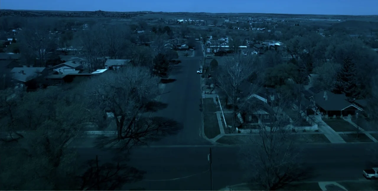 Alien Abduction: Travis Walton (2022) movie still: establishing — A suburban residential neighborhood with houses and trees sits under a night sky.…