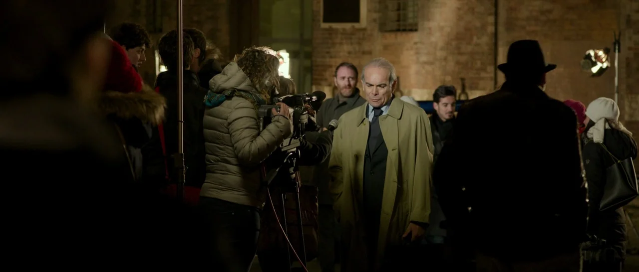 The Face of an Angel (2014) movie still: medium — An outdoor area at night is occupied by a group of cameramen and reporters. An older man in a…