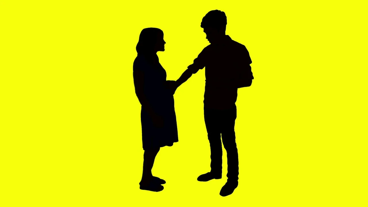 Tower (2016) movie still: fullbody — Two human figures stand against a bright, solid yellow background. A man reaches out to touch the rounded…