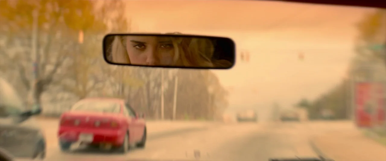 Baby Driver (2017) movie still: wide — A view from inside a car looking through the windshield at a road scene. The rearview mirror reflects a young…