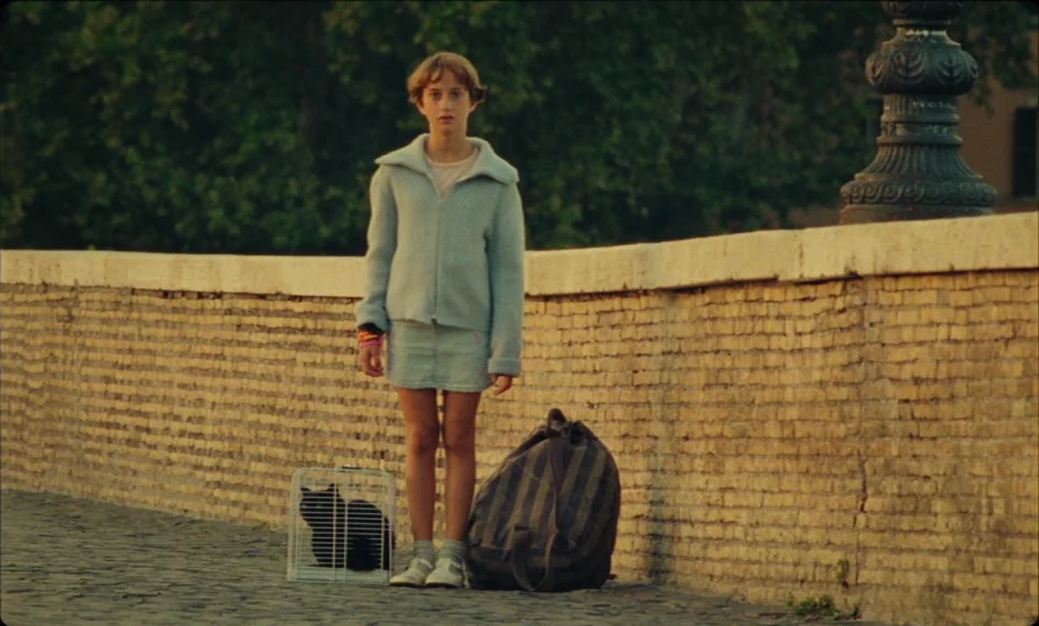 Misunderstood (2014) movie still: fullbody — A stone bridge with a brick parapet spans an area with greenery. A young girl stands on the pavement…
