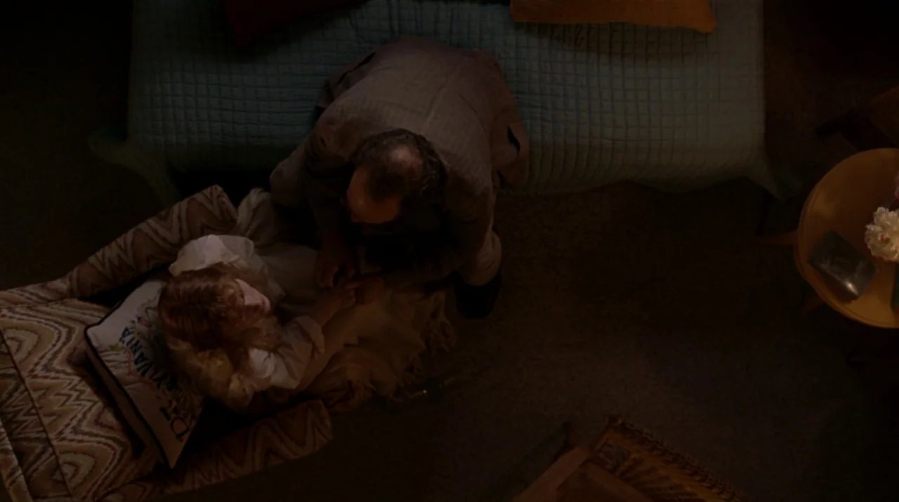 Lady in the Water (2006) movie still: wide — A furnished interior space with a teal-covered sofa and an upholstered chair. A man in a blazer kneels…