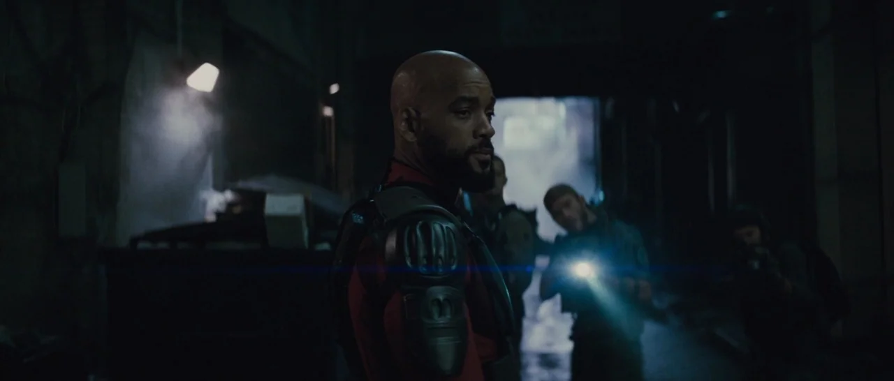 Suicide Squad (2016) movie still: medium — A narrow dark alley at night with industrial debris and shadows along the walls. A man in tactical armor…