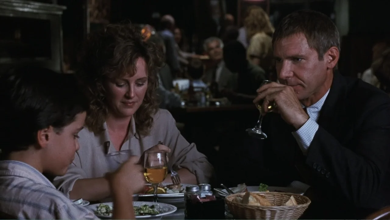 Presumed Innocent (1990) movie still: medium — A dimly lit restaurant interior with tables visible in the blurred background. A man, a woman, and a…