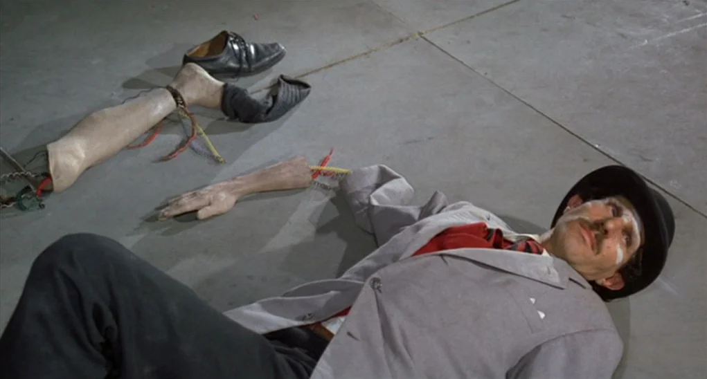 Dr. Goldfoot and the Girl Bombs (1966) movie still: medium — A man in a grey suit lies on a grey concrete floor. Beside him are a detached…