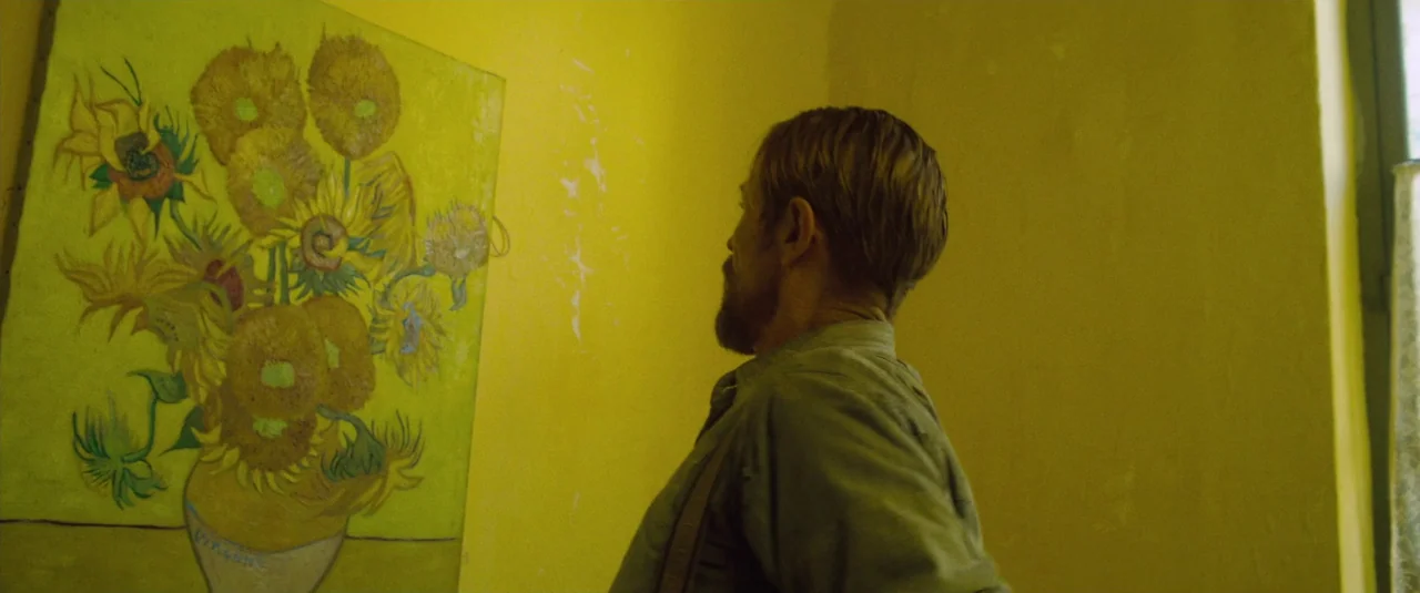At Eternity’s Gate (2018) movie still: medium — A small room features a vibrant sunflower painting hanging on a bright yellow wall. A man stands in…