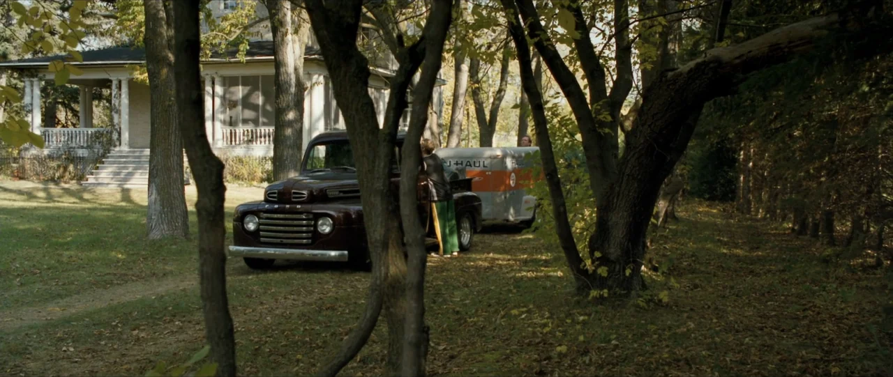 The Haunting in Connecticut (2009) movie still: wide — A rural property features a white wooden house near a gravel driveway with trees. A person…