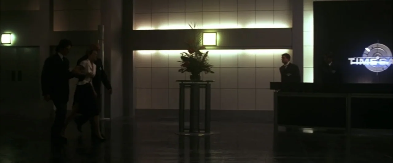 A Sound of Thunder (2005) movie still: wide — A spacious, dimly lit lobby features tiled walls, a central floral arrangement, and a desk. A man in a…