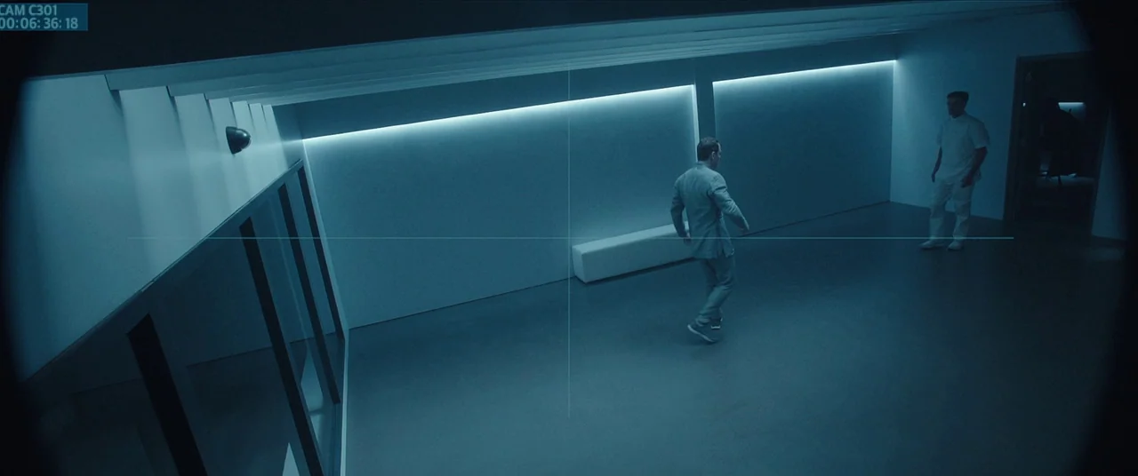 Assassin’s Creed (2016) movie still: wide — A sterile, windowless modern space features stark white walls and a smooth grey floor. One man in a grey…