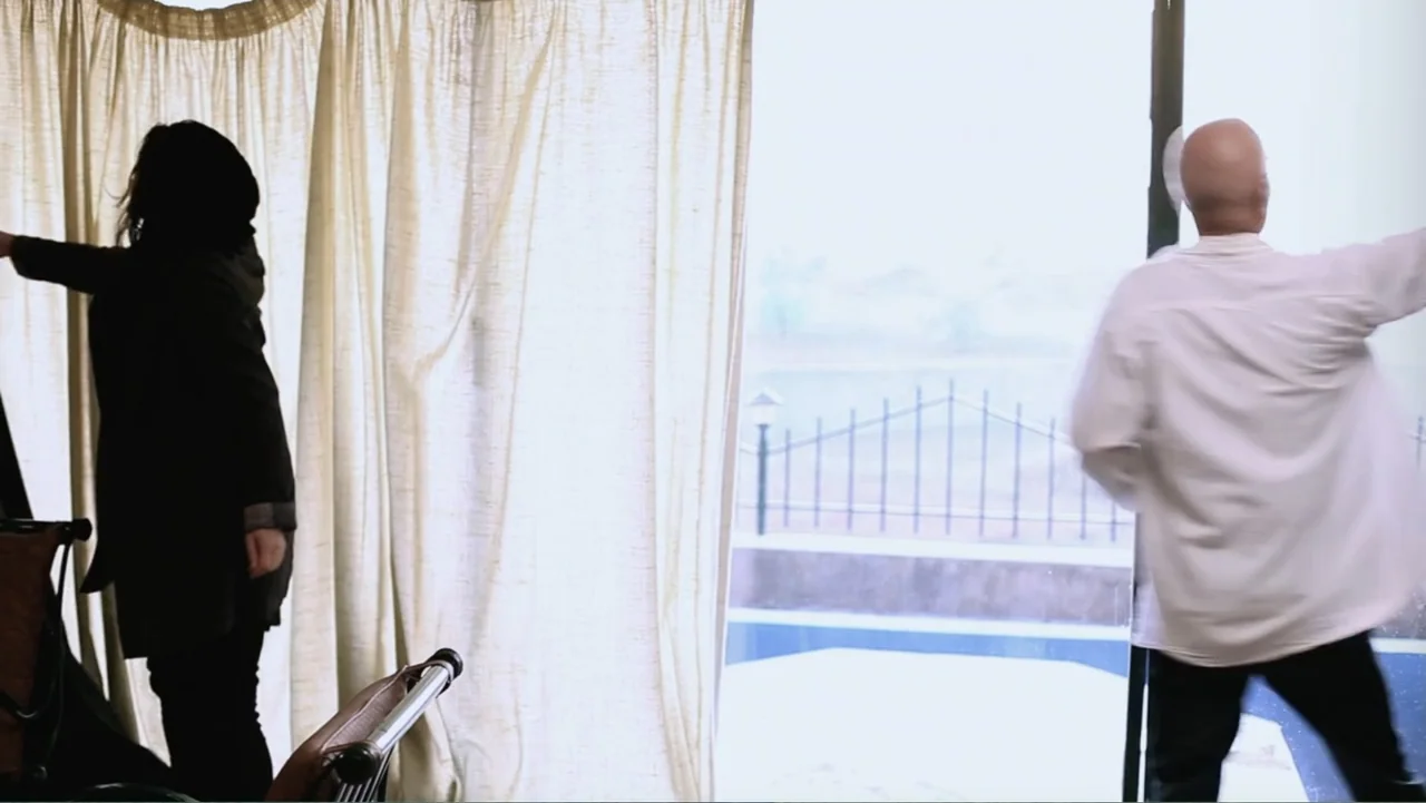 Closed Curtain (2013) movie still: medium — A light-filled room features a large window with sheer curtains looking onto a patio. Two figures stand…