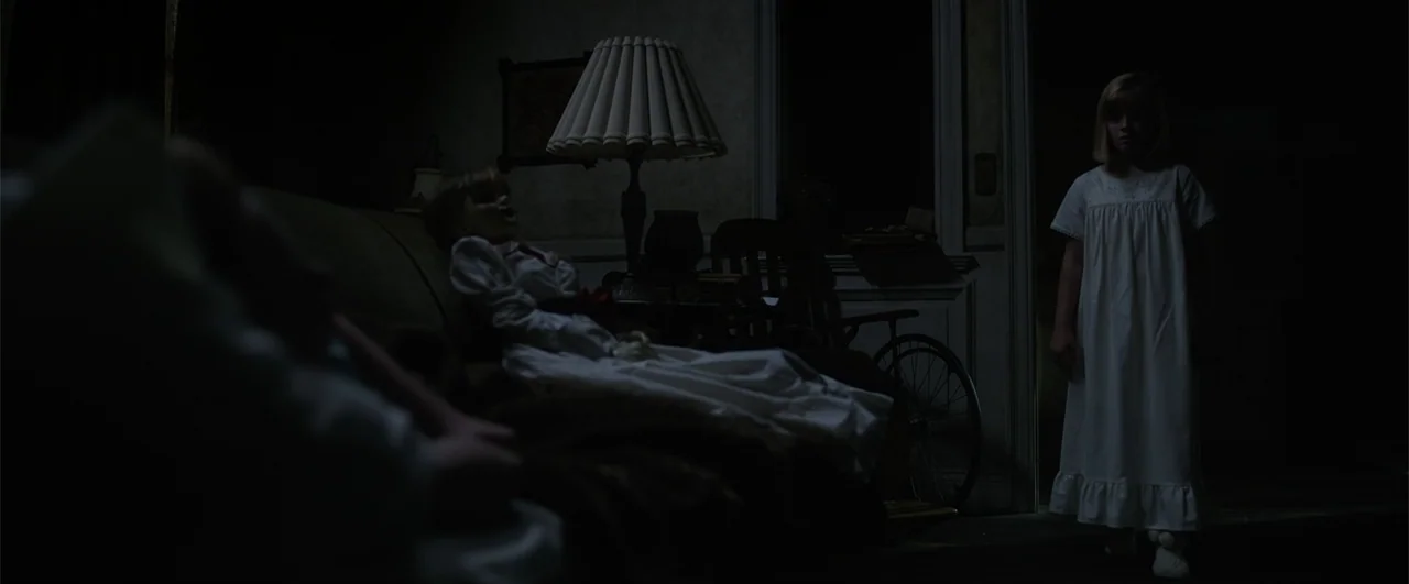 Annabelle: Creation (2017) movie still: wide — A dim, sparsely furnished room contains a vintage sofa with a seated porcelain doll. A young girl…