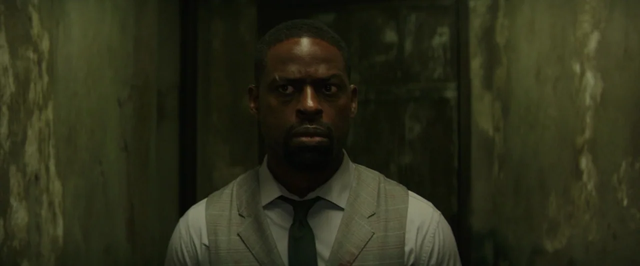 Hotel Artemis (2018) movie still: medium — A man stands in a dark, narrow corridor with peeling, grimy, mossy concrete walls. He stares forward…