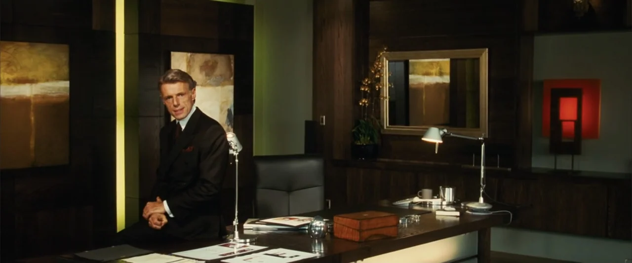 Catwoman (2004) movie still: medium — A high-end corporate office features dark wood paneled walls and modern abstract paintings. A man in a suit…