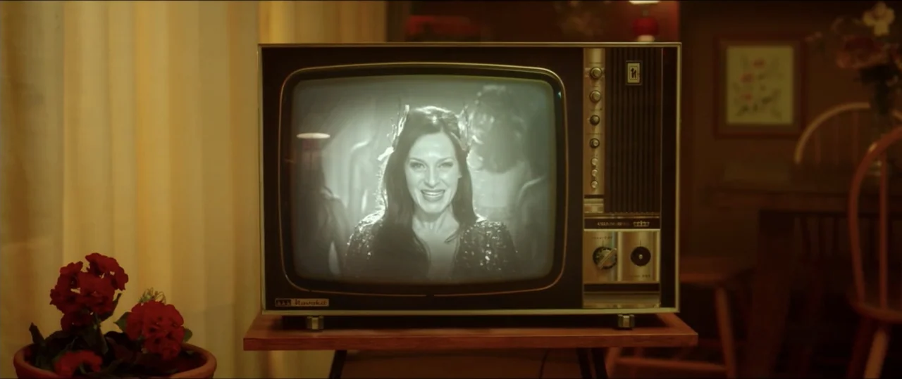 My Heart Goes Boom! (2020) movie still: medium — A retro-style television set sits on a small table in a dimly lit room. The screen displays a black…