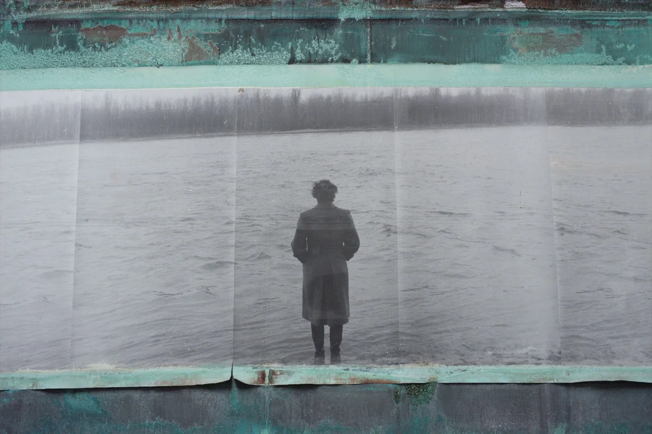 Anselm (2023) movie still: medium — A paper print featuring a figure is mounted on an oxidized copper wall. The central image shows a person…