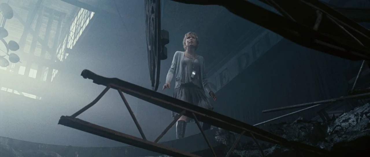 Silent Hill movie still: medium — A desolate, cavernous interior space is filled with twisted steel beams and heavy rubble. A young woman stands in…