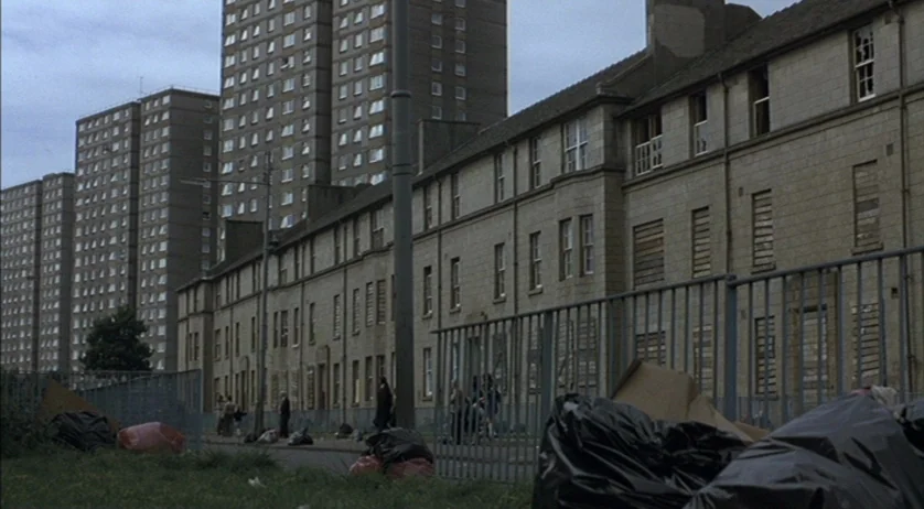 Ratcatcher (1999) movie still: wide — A dense urban housing complex features long rows of grey, boarded-up residential buildings. Tall residential…