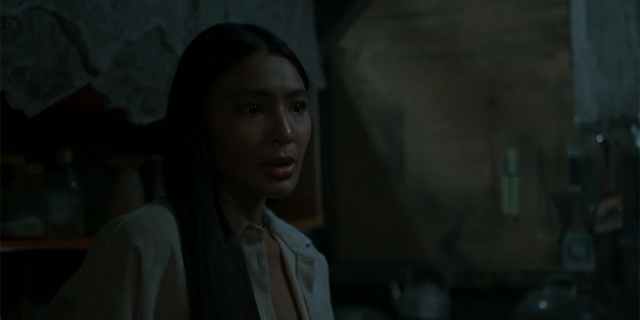 Nokturno (2024) movie still: medium — A dark, dimly lit kitchen with blurred shelves and cooking utensils in the background. A woman stands in the…