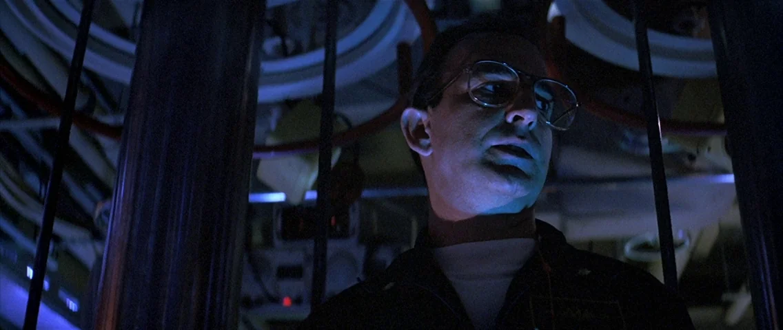 The Hunt for Red October (1990) movie still: medium — The interior of a cramped vessel is filled with pipes and metallic machinery. A man wearing…