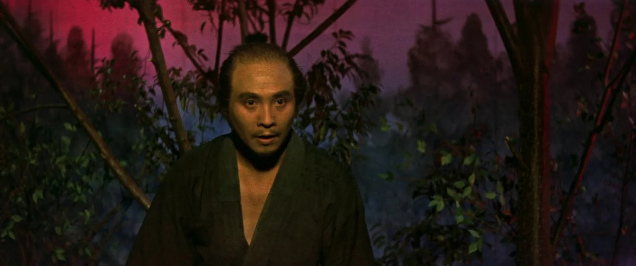 Ballad Of Narayama (1958) movie still: medium — A dense, dark forest setting appears at night with silhouetted trees against a red sky. A man in a…