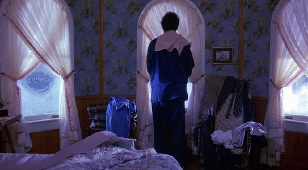 Groundhog Day (1993) movie still: medium — A bedroom features patterned wallpaper, arched windows, and a cluttered wooden chair. A man stands before…