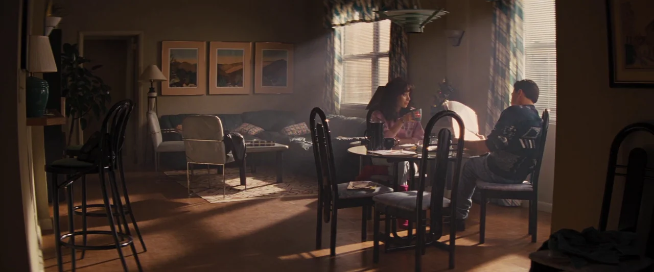 The Wolf of Wall Street (2013) movie still: wide — A 1990s living room features a round glass table and dark leather sofa. A man and a woman sit at…