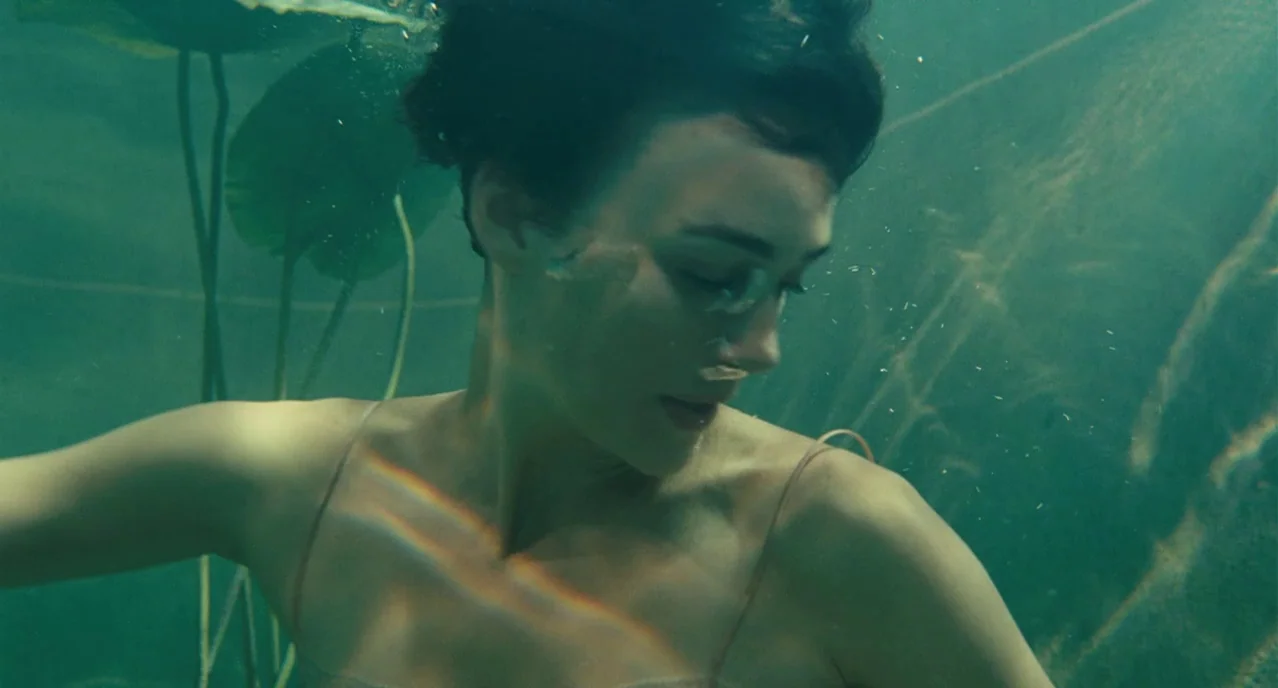 Atonement (2007) movie still: medium — A woman submerged in a murky pond with floating lily pads and underwater vegetation. The woman drifts slowly…