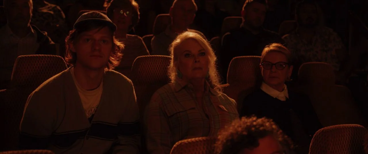 Let Them All Talk movie still: medium — Rows of dark upholstered seats filled with an audience in a dim room. Three distinct figures sit in the…
