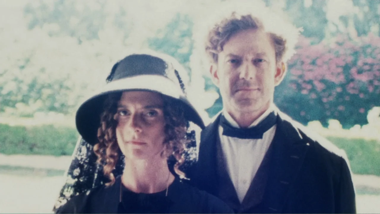 Demon in the White House (2021) movie still: medium — A sunny outdoor location features a man and woman dressed in 1900s attire. The pair stand side…