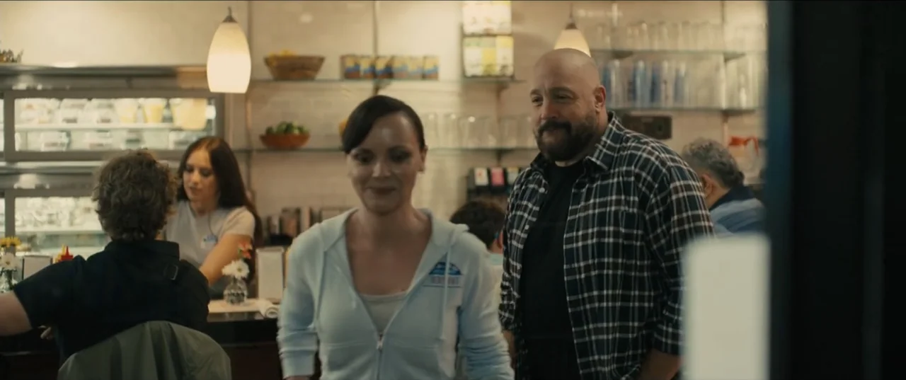 Guns Up (2025) movie still: medium — A well-lit casual diner interior features glass shelving with various glasses and decor. A man with a beard and…