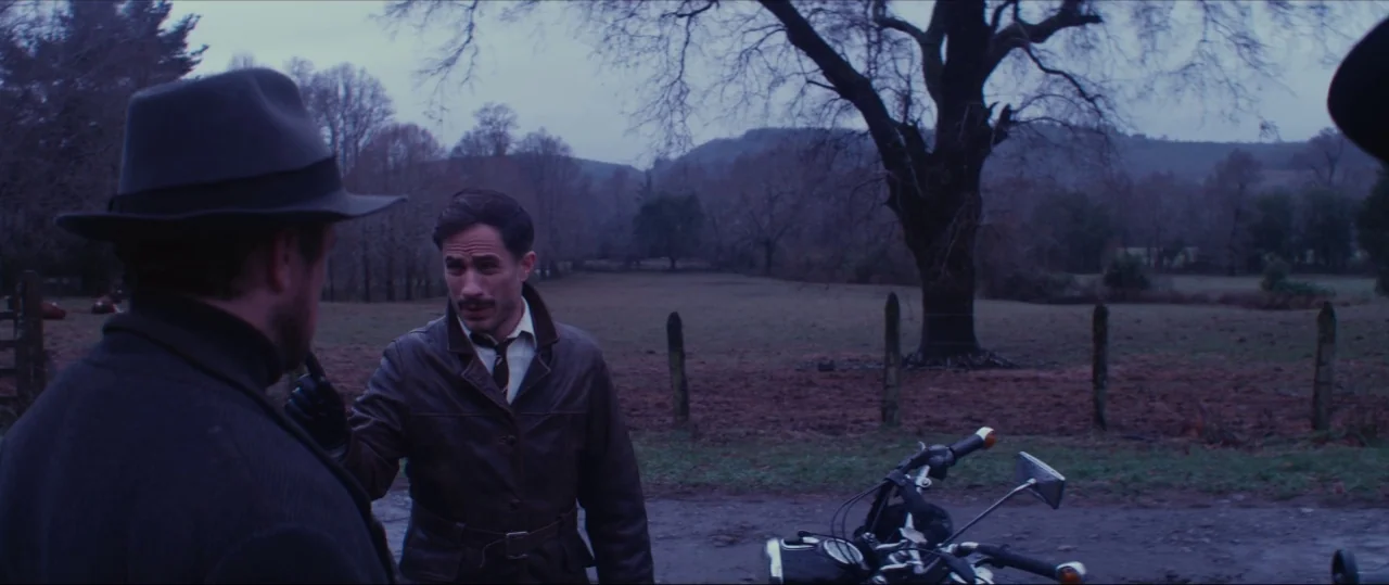 Neruda (2016) movie still: medium — A rural landscape features a leafless tree standing before a field and barbed wire. Two men stand facing each…
