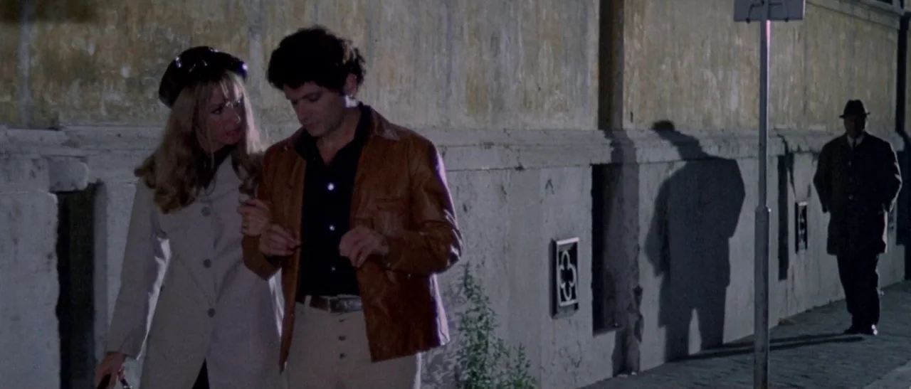 The Bird With The Crystal Plumage (1970) movie still: medium — A stucco wall lines a dark sidewalk at night under artificial illumination. A young…