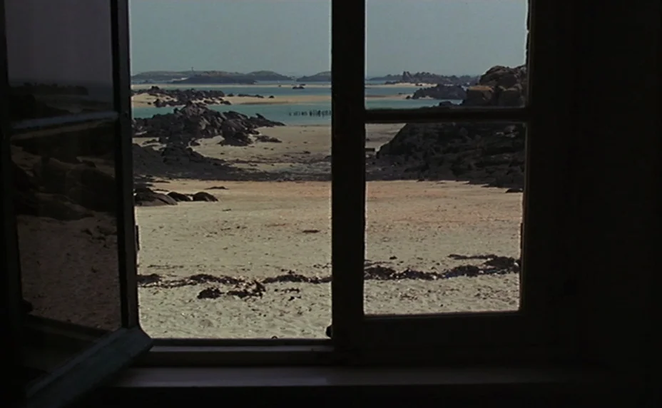 Kung Fu Master! (1988) movie still: establishing — A view through an open wooden window frames a rocky coastal beach. Sandy dunes and dark rock…