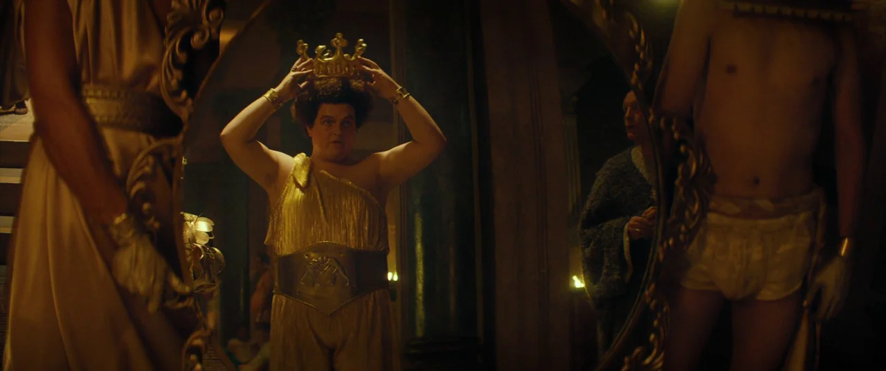 Seneca: On The Creation Of Earthquakes (2023) movie still: medium — A dimly lit room with ornate gold furniture and a large oval mirror. A man…