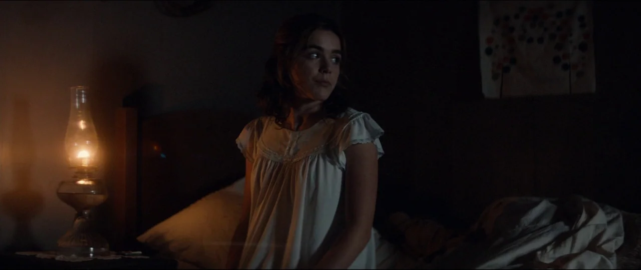 One & Two (2015) movie still: medium — A dark, spartan room features a wooden headboard and an illuminated oil lamp. A young woman in a white…