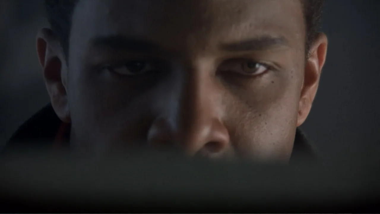 Crisis Point (2012) movie still: closeup — A close view of a man's face set against a dark, indistinct background. The subject stares forward while…