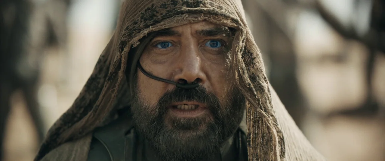 Dune: Part 2 (2024) movie still: closeup — A man stands in a desolate desert environment while wearing a draped fabric head covering. He stares…