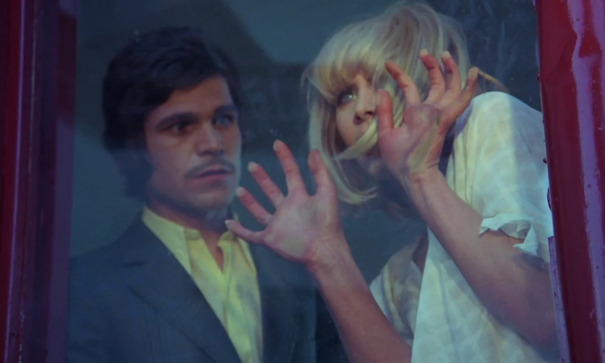 Vampyros Lesbos (1971) movie still: medium — Two individuals look through a glass panel into a dark space. A woman presses her hands against the…