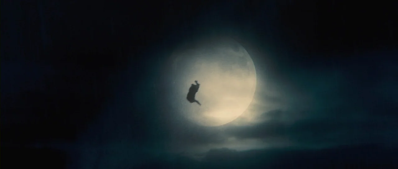 Grabbers (2012) movie still: wide — A dark night sky dominated by a large, glowing full moon partially obscured by clouds. A small silhouette of a…