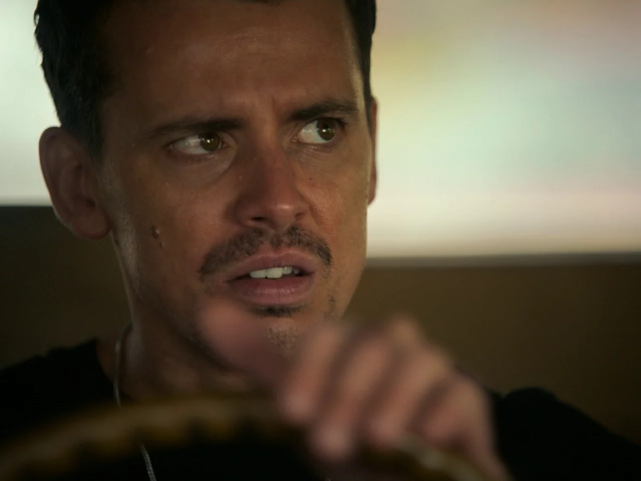Of An Age (2022) movie still: closeup — The interior of a vehicle at night with blurred light reflections on the windows. A man with a thin mustache…