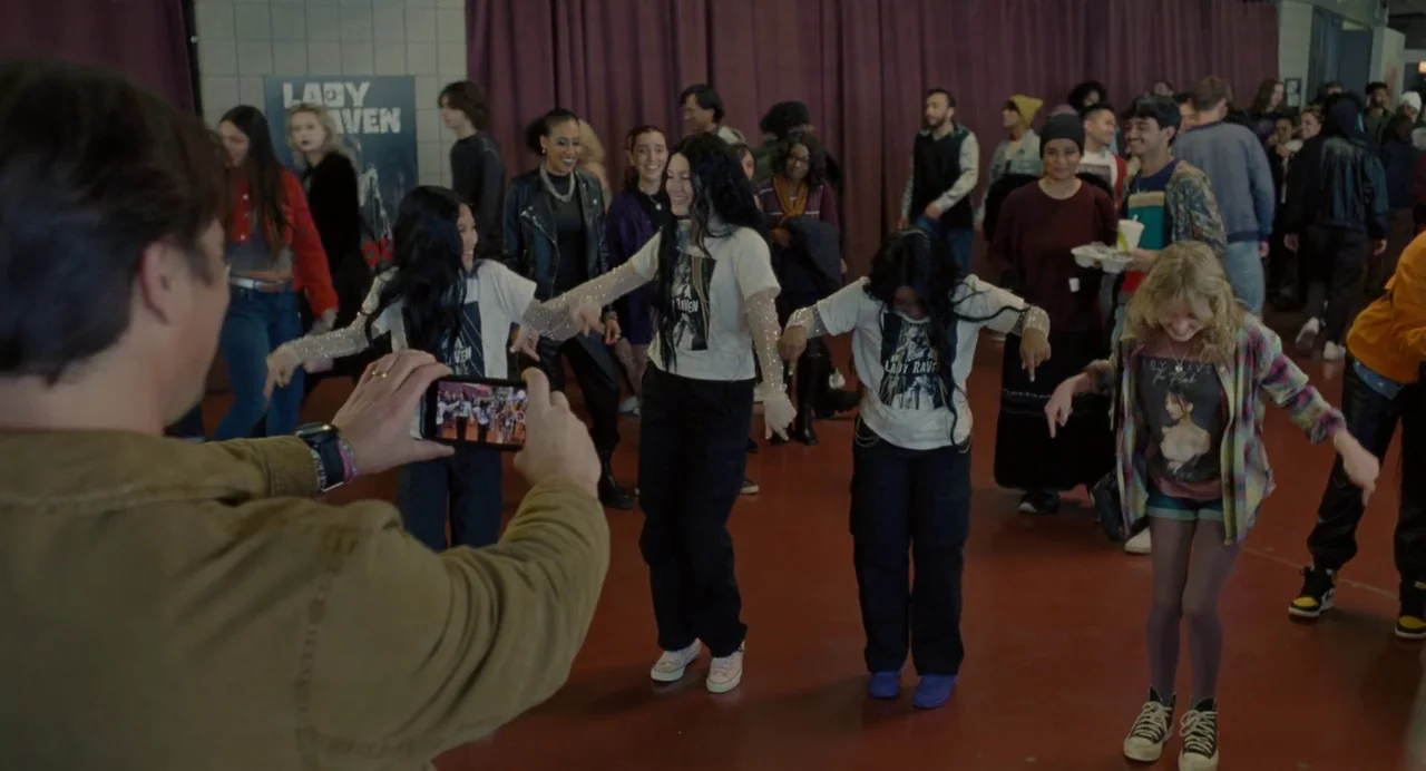 Trap (2024) movie still: medium — An interior school hallway with purple curtains draped against a brick wall background. Several teenagers…