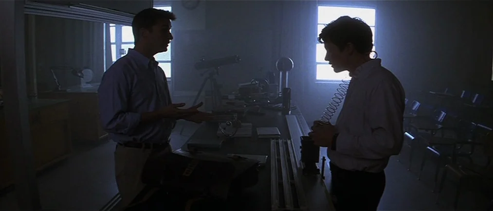 Donnie Darko movie still: medium — A dark science laboratory filled with equipment features two men engaged in a discussion. The room is backlit by…